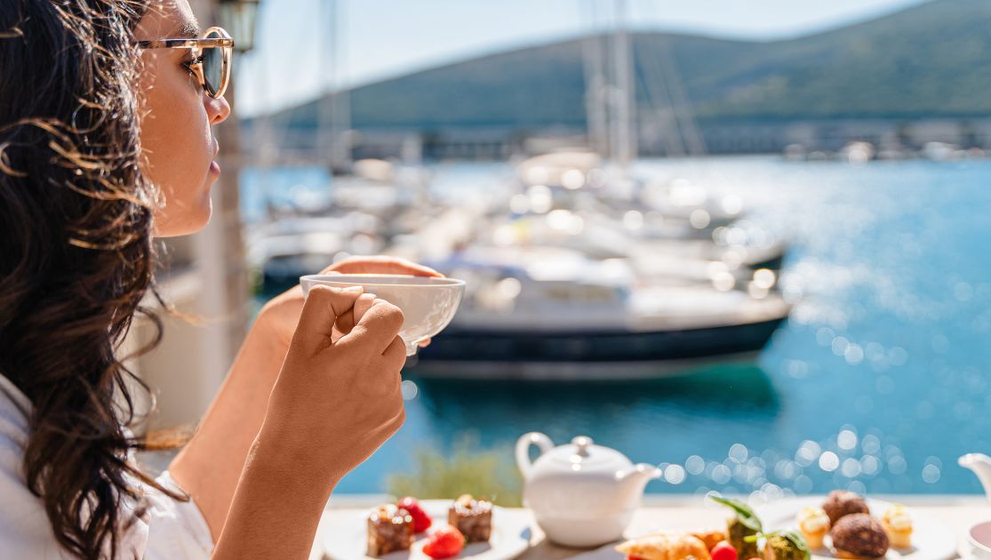 A Woman Sitting At A Table Enjoying her breakfast with a sea view under the rays of the sun at chedi lustica bay